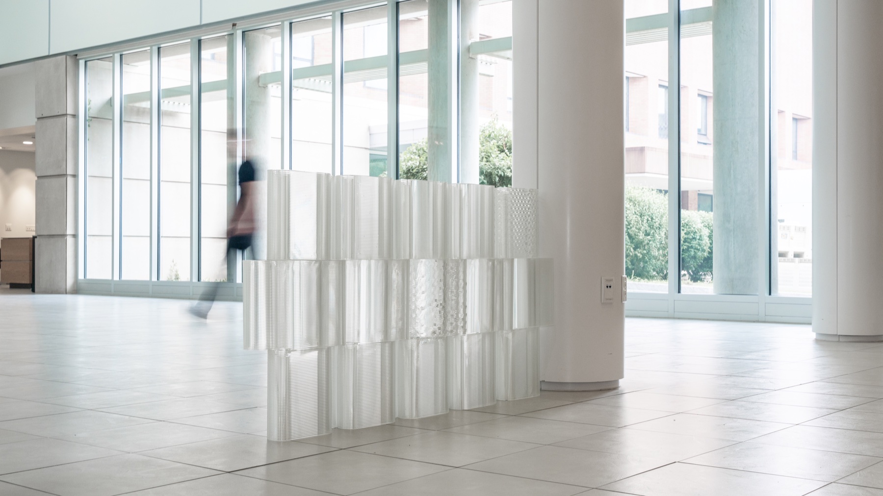A freestanding dry-stacked wall of interlocking glass bricks in a daylit atrium